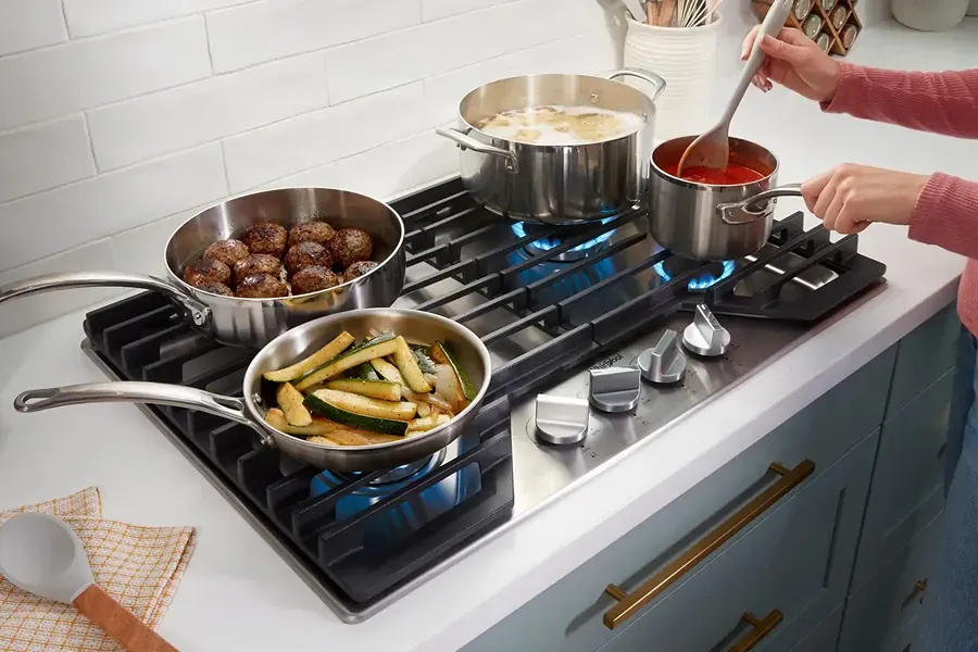 Person cooking on a Whirlpool 5-burner gas cooktop with continuous grates for serious home chef features.